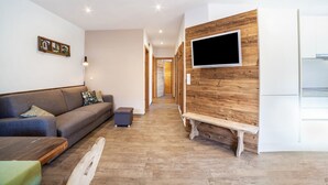 A modern living room with a sofa, a bench, a TV mounted on a wooden wall, and a hallway leading to another room.