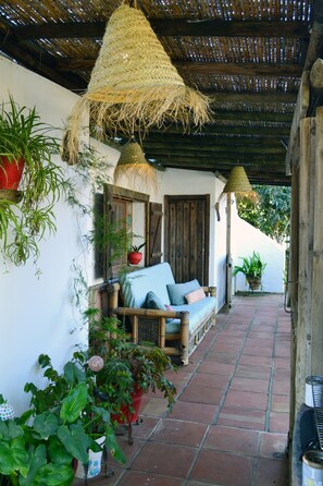 Un espacio de descanso techado al aire libre con sofá, plantas en macetas y lámparas colgantes.