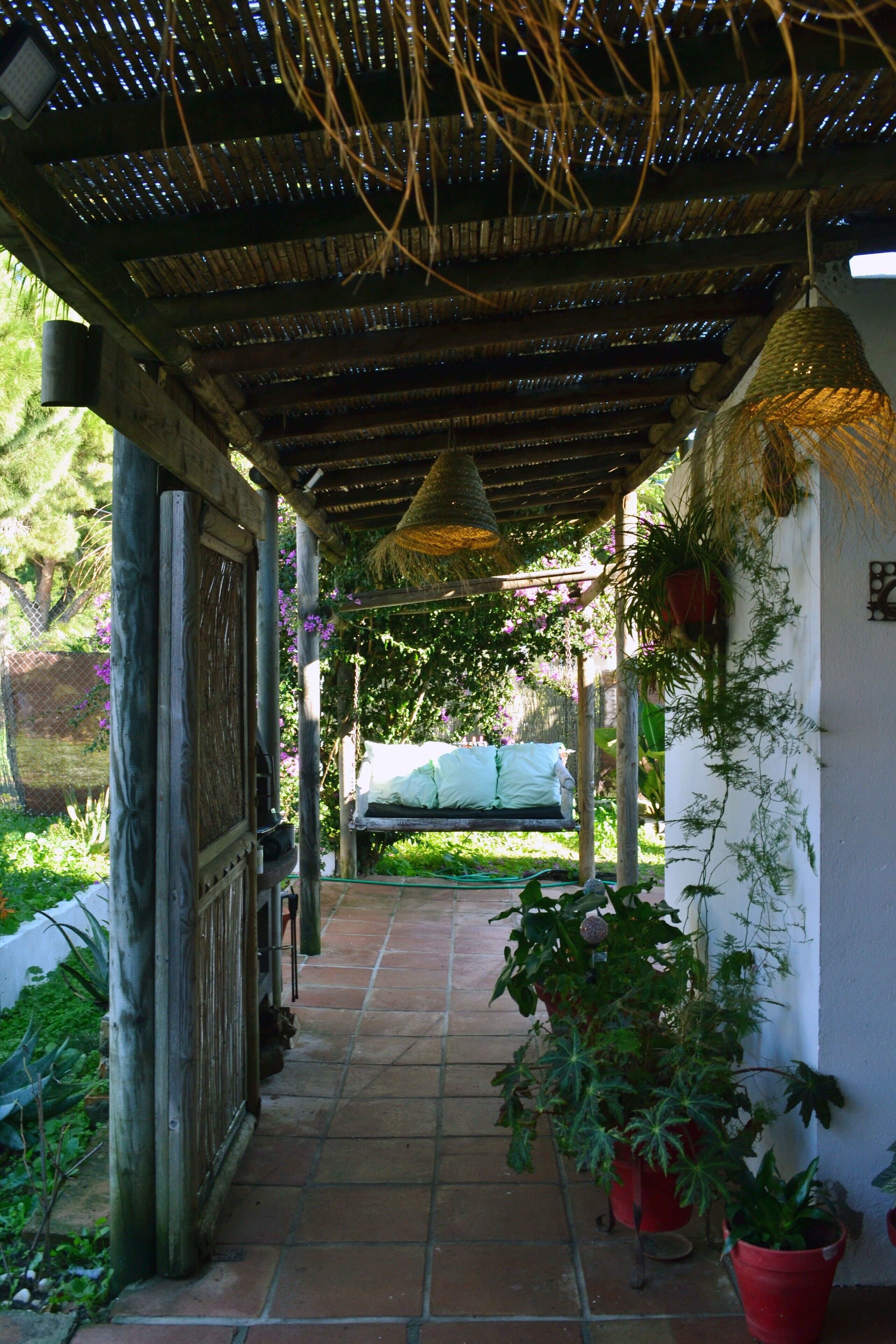 A covered outdoor area with a tiled floor, wooden pillars, and hanging plants.