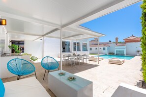 A modern outdoor patio with a pool, white furniture, and a clear view of the surrounding architecture.