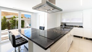 Uma cozinha moderna com uma ilha grande, armários brancos e vista para o exterior.