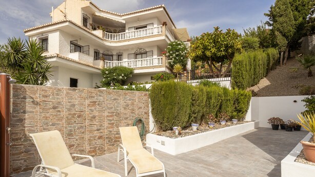 A multi-story building with balconies, a stone wall, and a patio area with two lounge chairs. - Holiday Home Casa Curumbico with Sea & Mountain View, Garden and Wi-Fi (Almunecar)