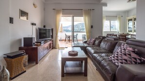 A living room with a television, sofa, coffee table, and a view of the outdoors. - Holiday Home Casa Curumbico with Sea & Mountain View, Garden and Wi-Fi (Almunecar)