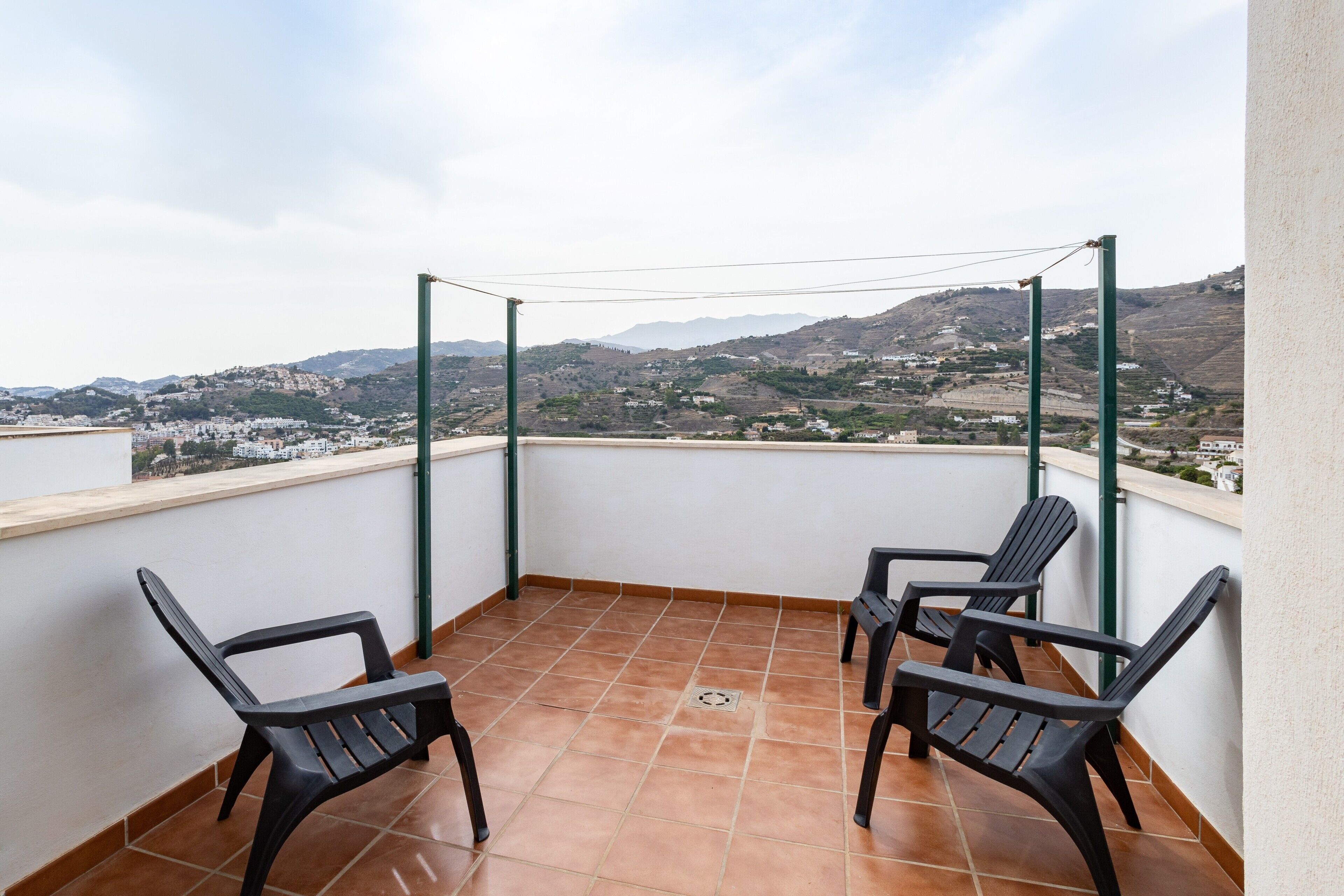 Un balcon avec deux chaises, une pergola en métal et une vue sur un paysage vallonné.