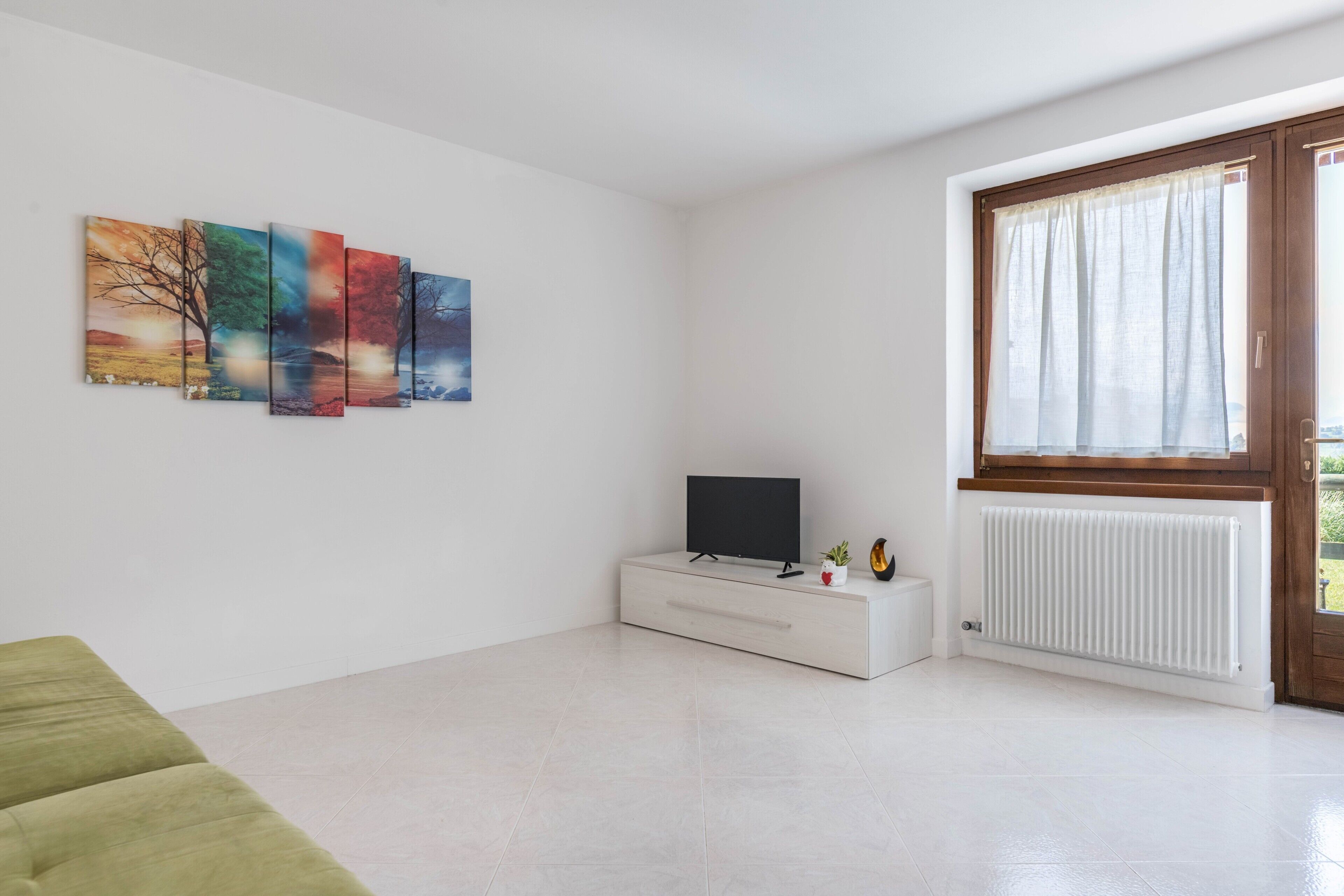 Een moderne woonkamer met een flatscreen televisie, een witte radiator en een raam met gordijnen.