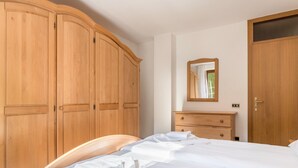 Un dormitorio con cama, armario de madera, cómoda y espejo en la pared.