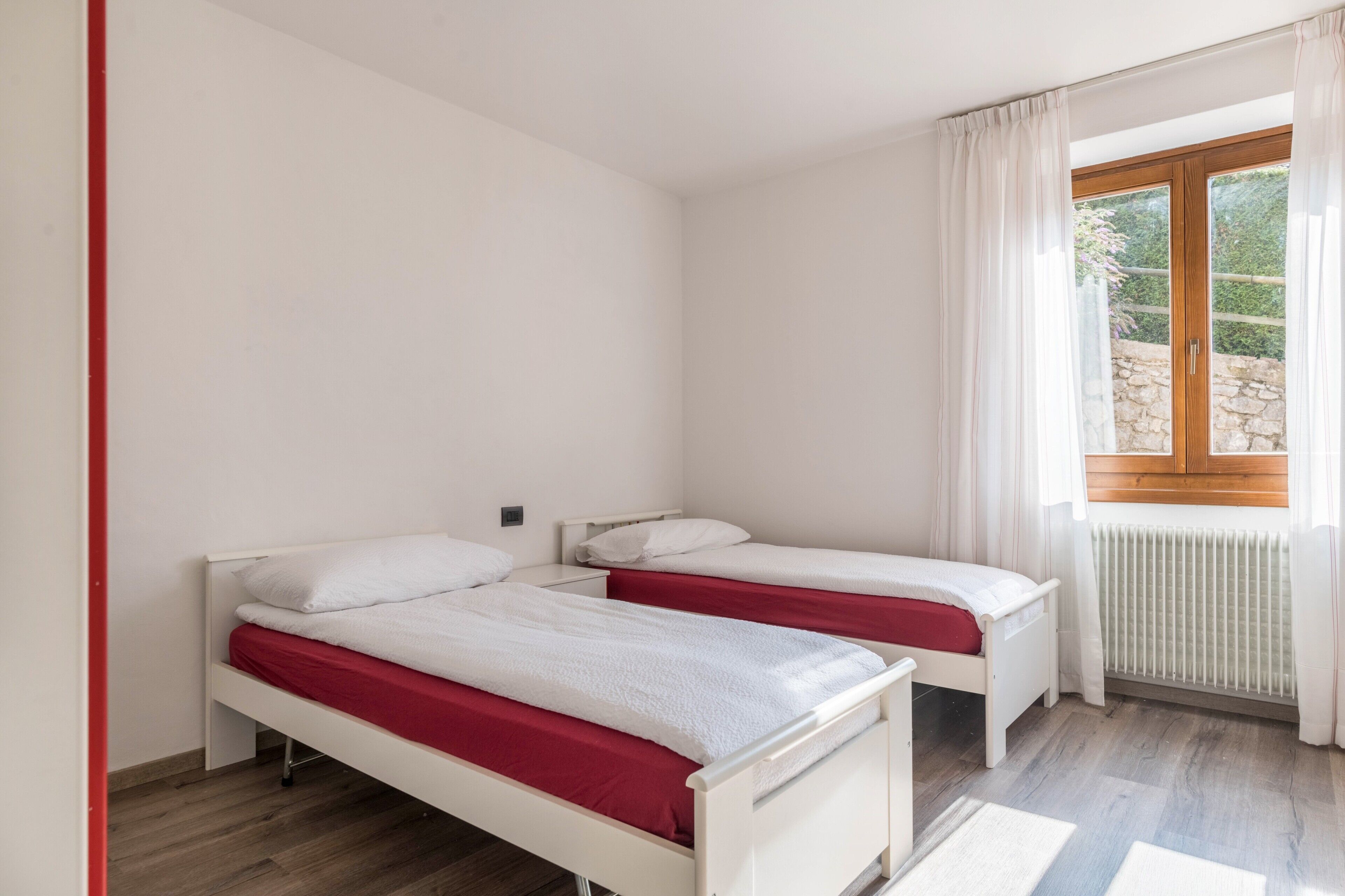 Une chambre avec deux lits simples, une fenêtre avec des rideaux, un radiateur et un mur en pierre à l’extérieur.