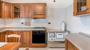 Una cocina con armarios de madera, estufa a gas, horno empotrado y salpicadero de azulejos blancos.