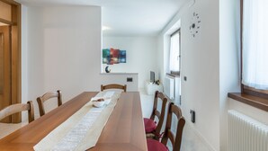 Un comedor con una mesa de madera, sillas, un reloj de pared blanco y una ventana con cortinas.