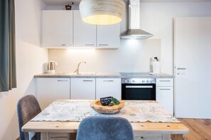 Une cuisine moderne avec des meubles blancs, une table en bois recouverte d’une nappe à motifs floraux et un luminaire suspendu.