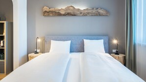 Habitación de hotel con una cama grande, dos mesitas de noche con lámparas, una obra de arte en la pared y una mesita auxiliar de madera.