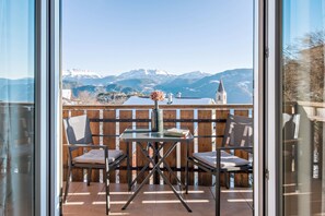 A balcony with a table and chairs, a vase with flowers, and a view of snow-capped mountains.