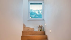 A wooden staircase with a window above it, a small table with a lamp, and a wall-mounted light fixture. - Apartment 'Villa KaTo' with Lake View, Garden & Terrace (Kaltern an der Weinstraße)