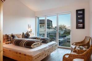 A bedroom with a wooden bed, a large window, wicker chairs, and a view of a building.