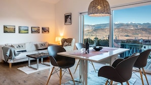 A modern living room with a dining area, large windows, and mountain views. - Apartment 'Villa KaTo' with Lake View, Garden & Terrace (Kaltern an der Weinstraße)