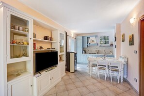 Una cocina con gabinetes blancos, un televisor y un comedor con sillas y una mesa.
