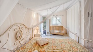 A bedroom with a canopy bed, a crib, and a sliding glass door leading to a balcony. - Holiday Home 'Paola E Del Poeta' with Shared Pool, Private Garden and Wi-Fi (Dolcedo)