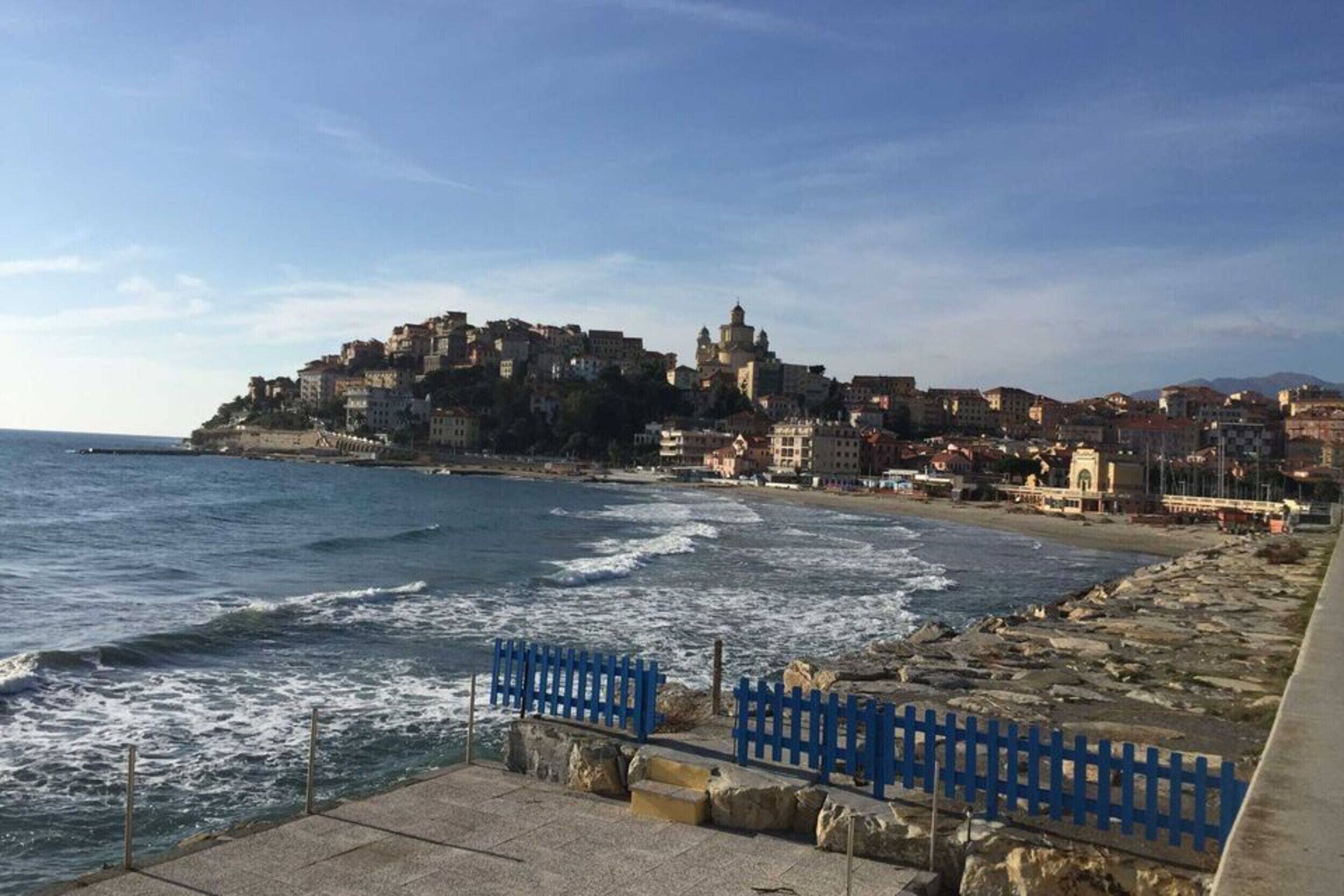Un paisaje urbano costero con un edificio destacado en la cima de una colina, una playa y un litoral rocoso.