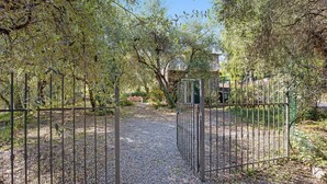 A gravel pathway leading through a metal gate surrounded by trees and greenery. - Holiday Home 'Paola E Del Poeta' with Shared Pool, Private Garden and Wi-Fi (Dolcedo)