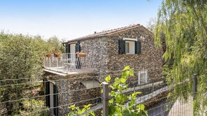 A stone house with a balcony, surrounded by greenery. - Holiday Home 'Paola E Del Poeta' with Shared Pool, Private Garden and Wi-Fi (Dolcedo)