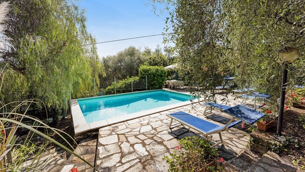 A swimming pool with stone flooring, surrounded by greenery and outdoor furniture. - Holiday Home 'Paola E Del Poeta' with Shared Pool, Private Garden and Wi-Fi (Dolcedo)