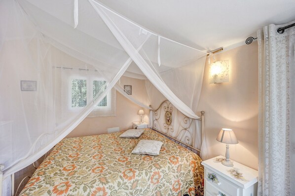 A bedroom with a canopy bed, bedside lamps, a nightstand, and a window with curtains.