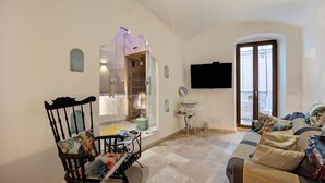 Una sala de estar con un sofá, una silla, un televisor y una ventana con cortinas.