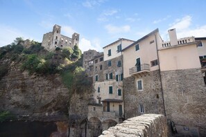 Un pueblo costero con edificios históricos de piedra, un castillo imponente en un acantilado y un puente de piedra.