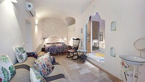 Un dormitorio con cama, sofá, sillón, una mesita y baño con lavabo y espejo.