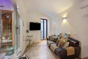 Una sala de estar con un sofá, un televisor, cabina de ducha de vidrio y una mesita.
