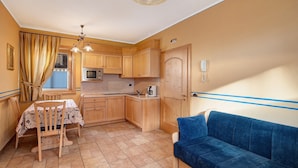 A compact kitchen with wooden cabinets, a dining table with chairs, a blue sofa, and a chandelier. - Chalet Betty Appartamento Pec with Mountain View (Livigno)