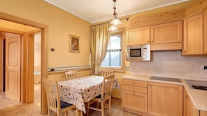 A kitchen with wooden cabinets, a microwave, a dining table with chairs, and a window with curtains. - Chalet Betty Appartamento Pec with Mountain View (Livigno)
