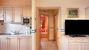 A kitchen with wooden cabinets, a microwave, a coffee maker, and a TV on a stand. - Chalet Betty Apartment Muf with Mountain View, Wi-Fi, Balcony & Garden (Livigno)