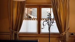 A room with a large window, curtains, a bench, and a floor lamp. - Chalet Betty Apartment Muf with Mountain View, Wi-Fi, Balcony & Garden (Livigno)