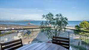 Een balkon met uitzicht op het strand en de oceaan, houten meubels en een bloempot.