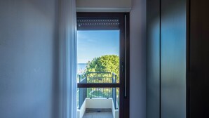 Een uitzicht door een deur op een balkon met een hekwerk, een heldere lucht en een verre boom.