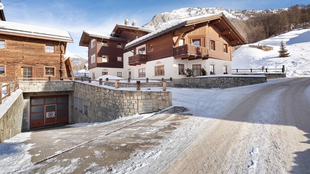 A wooden chalet with a stone entrance, a balcony, and a view of a snowy mountain. - Chalet Betty Apartment Sgembro with Mountain View (Livigno)