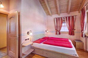 A bedroom with a bed, bedside tables, a wooden door, a window with curtains, and a wooden ceiling.