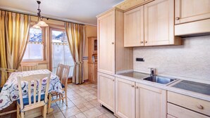 A kitchen with wooden cabinets, a sink, and a dining area with a table and chairs. - Chalet Betty Apartment Sgembro with Mountain View (Livigno)