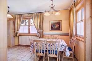 A dining area with a table set for four, wooden chairs, a chandelier, and a painting on the wall.