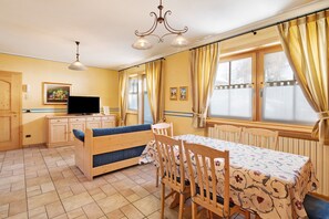 A cozy room with a sofa, a dining table, a television, and a window with curtains.
