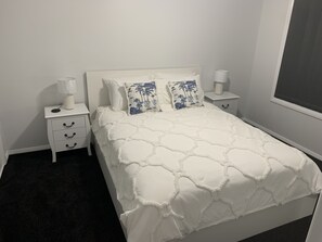 A bedroom with a white bed, two nightstands, and a window.