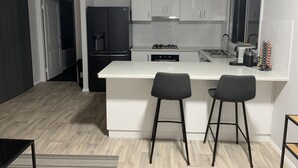 A modern kitchen with white cabinets, a black refrigerator, a gas stove, and two bar stools. - YARRAWONGA PARK COTTAGE<br>Cozy 2 bedroom cottage on small acreage  (Mudgee)