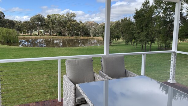 A covered outdoor seating area with a table and chairs, overlooking a grassy field and a body of water. - YARRAWONGA PARK COTTAGE<br>Cozy 2 bedroom cottage on small acreage  (Mudgee)
