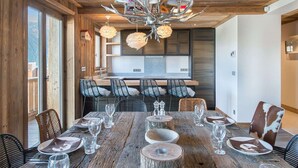 A rustic dining area with a wooden table set for six, surrounded by chairs with fur throw cushions. A unique chandelier with colorful floral designs hangs above. - 4-bedroom apartment for 10 in central Courchevel 1850 (Courchevel 1850)