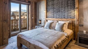 A rustic wooden bedroom with a large bed, a stone wall, and a view of a wooden cabin through a sliding door. - 4-bedroom apartment for 10 in central Courchevel 1850 (Courchevel 1850)