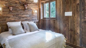 A rustic room with a wooden ceiling, a bed with white bedding, and two mounted animal heads on the wall. - 4-bedroom apartment for 10 in central Courchevel 1850 (Courchevel 1850)