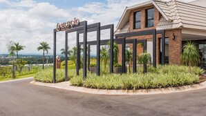 A hotel entrance with a sign reading 'RECEPTION TO,' surrounded by landscaped greenery and a view of distant hills.