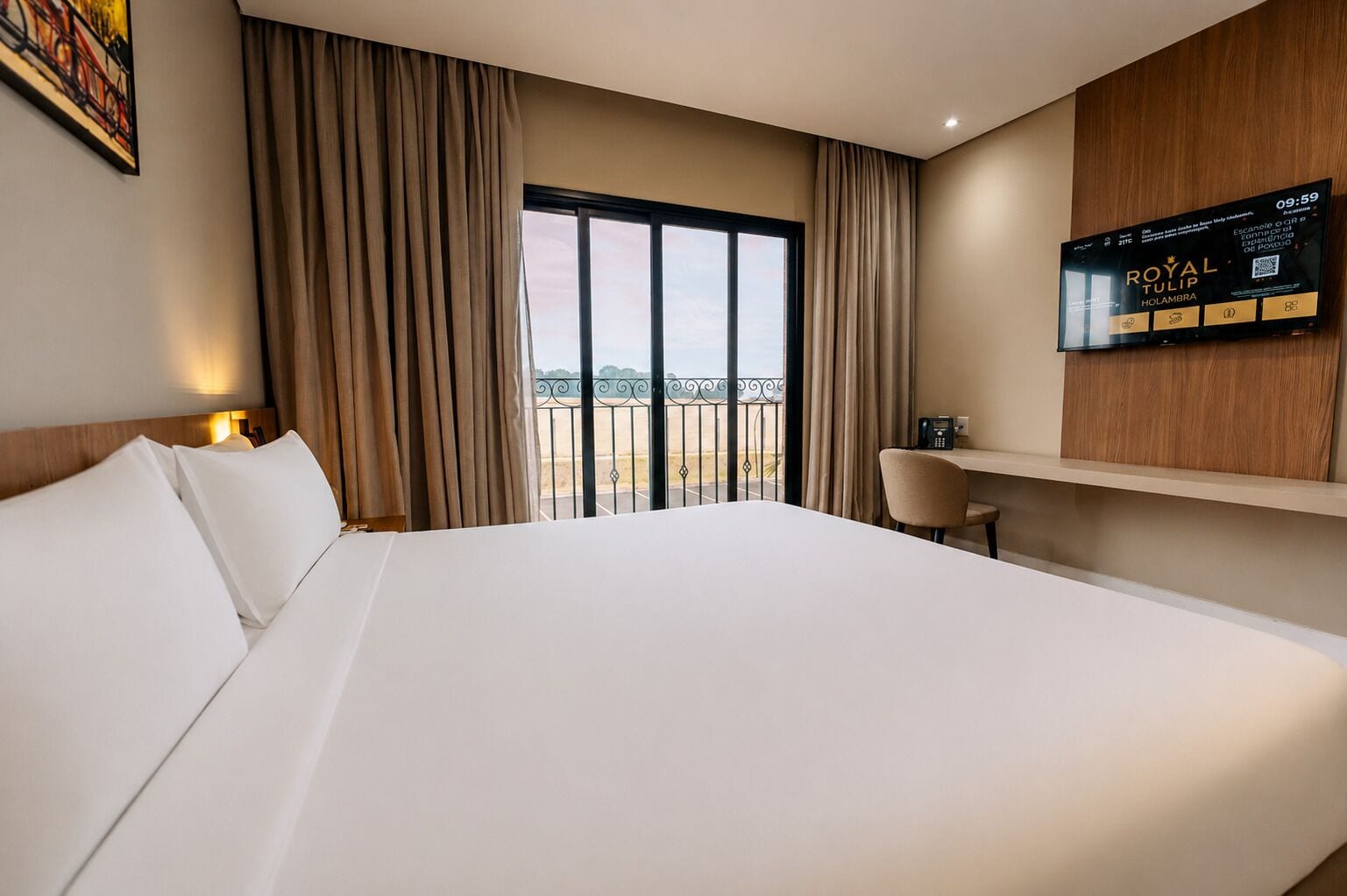 Ein Hotelzimmer mit einem großen Bett, einem Schreibtisch, einem Fernseher und einem Balkon mit Blick.