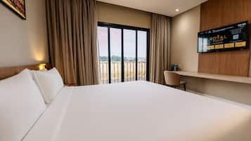 Ein Hotelzimmer mit einem großen Bett, einem Schreibtisch, einem Fernseher und einem Balkon mit Blick.